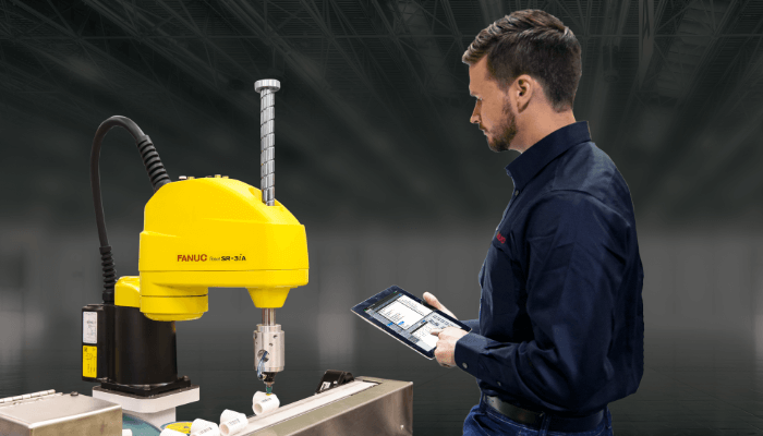 Engineer monitoring a FANUC robotic arm using a tablet to improve production efficiency and reduce machine downtime through automation engineering solutions.